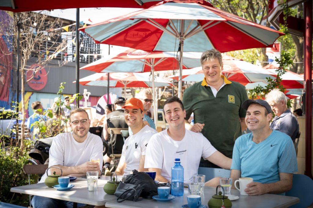 Café: "Friends laughing around a café table under red and white umbrellas in Hazelwood."Workshop17 coming soon